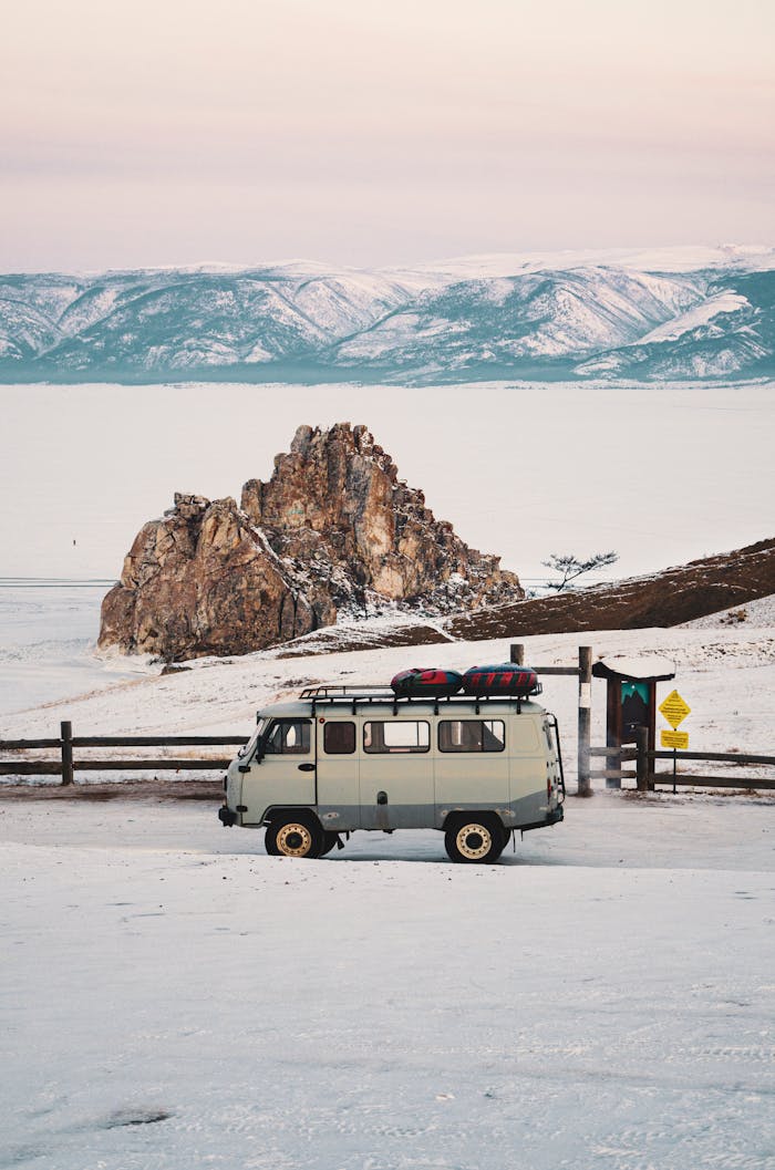 A classic camper van parked in a scenic winter landscape with snowcapped mountains in the background.