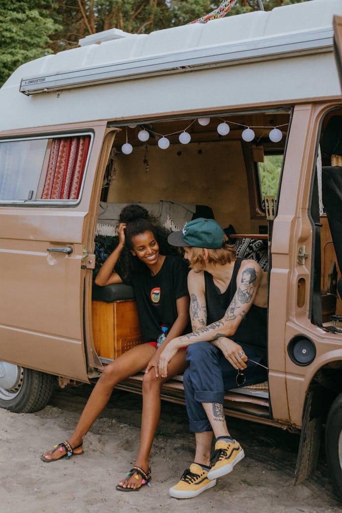 Two friends enjoying a road trip, relaxing by their vintage camper van in nature.
